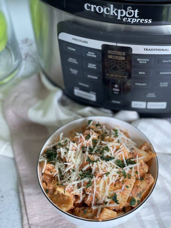 a bowl of pressure cooker lazy lasagna topped with shredded cheese and fresh herbs with a crockpot express pressure cooker in the background
