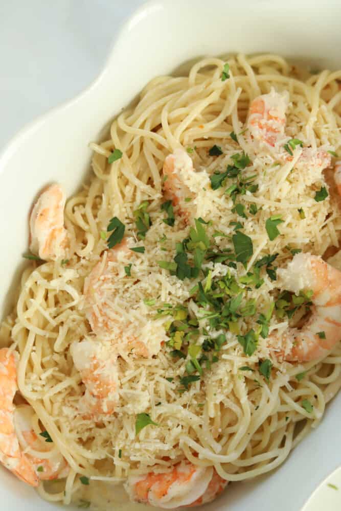 overhead image of a white baking dish with cooked spaghetti noodles, shrimp, Parmesan, and parsley that have been baked in the oven for garlic shrimp scampi
