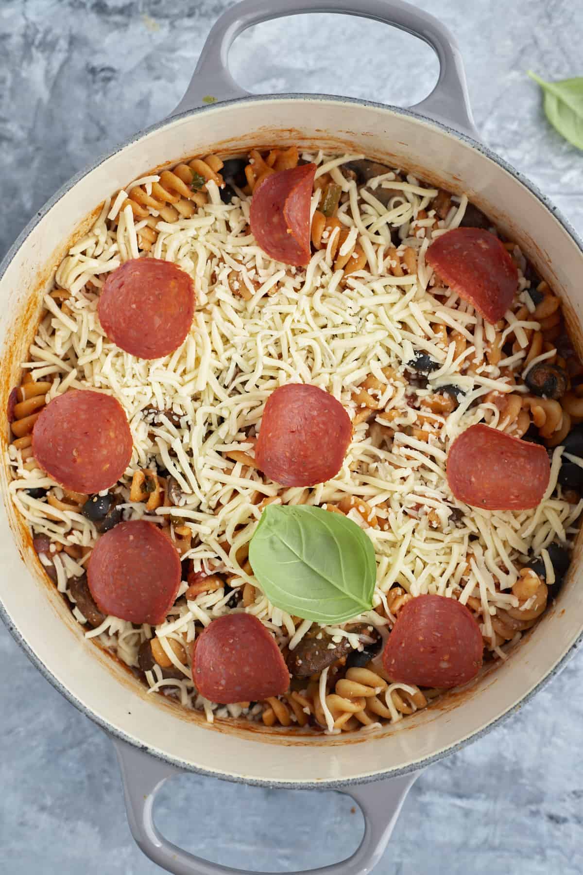 overhead image of a pot full of pizza pasta topped with cheese and pepperoni