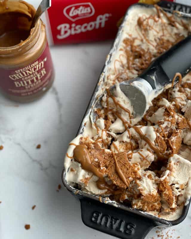 overhead image of a loaf pan full of no churn Biscoff ice cream with a tub of cookie butter and a box of Biscoff cookies on the side