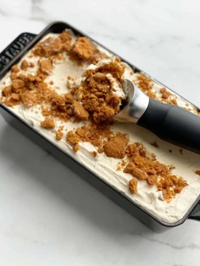 a loaf pan full of no churn biscoff ice cream with an ice cream scoop dipping out a portion