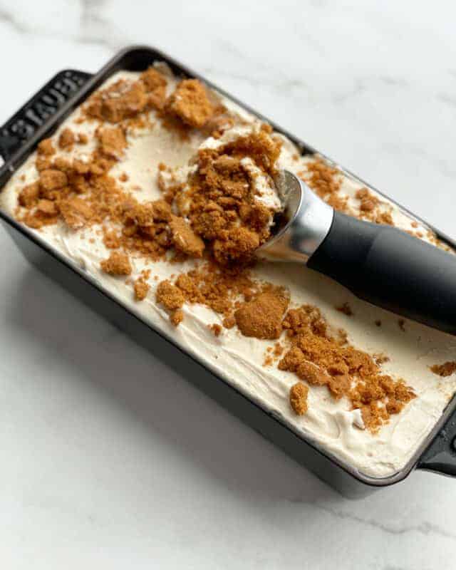 a loaf pan full of no churn biscoff ice cream with an ice cream scoop dipping out a portion