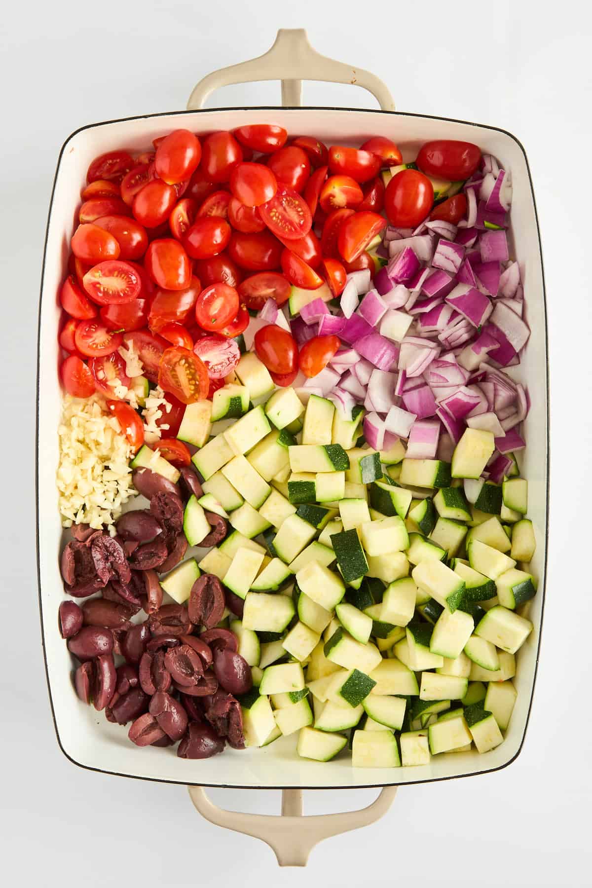 Tomatoes, red onion, zucchini, olives, and garlic in a baking dish. 