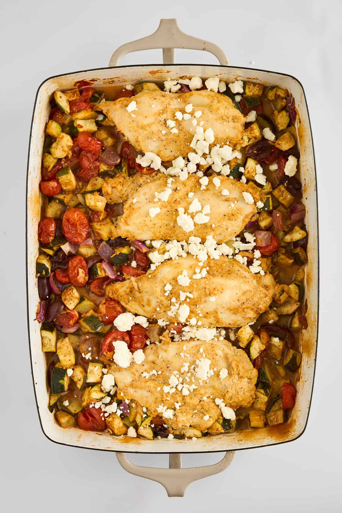 Hummus Baked Chicken in a baking dish with veggies topped with feta. 