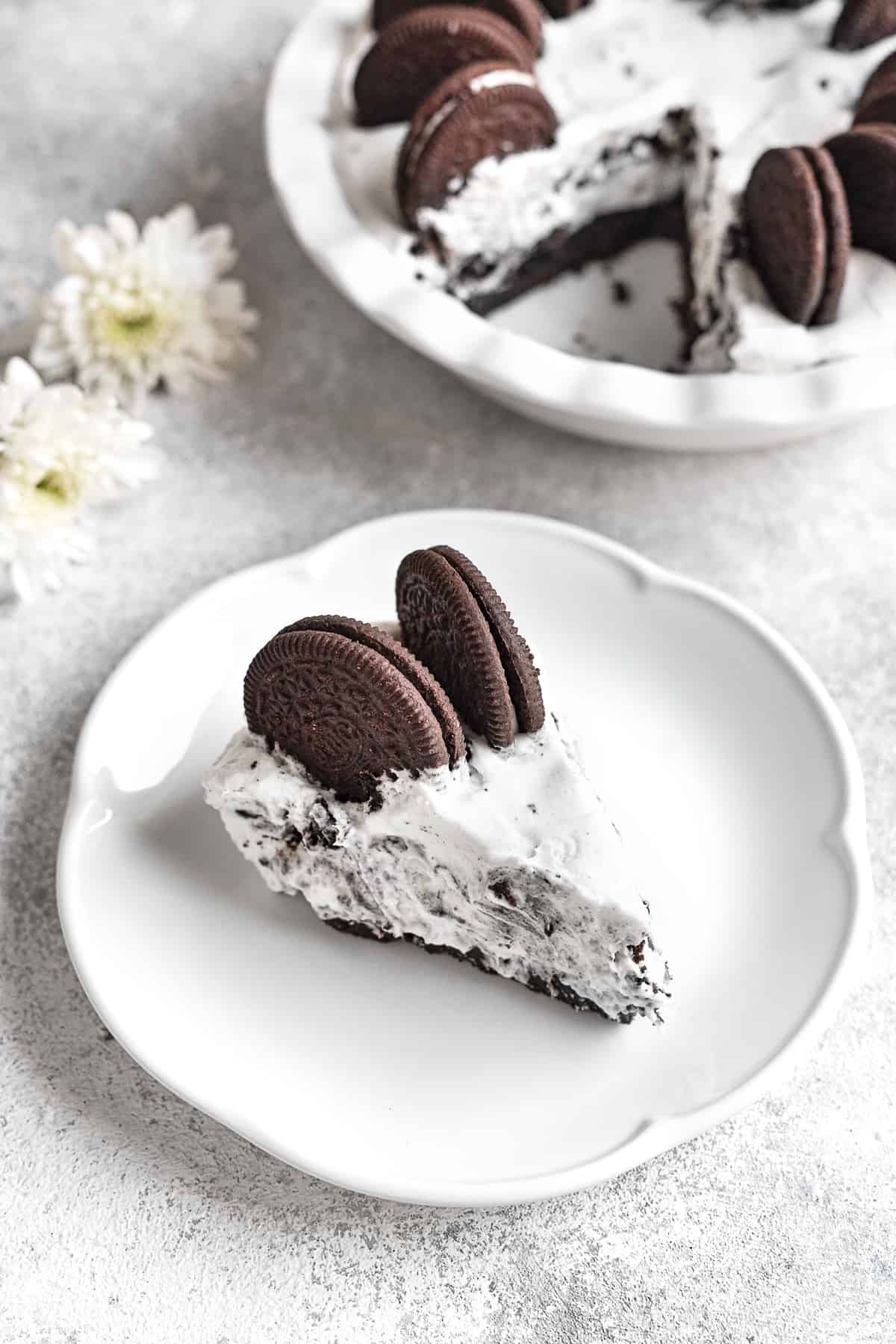 a piece of no-bake Oreo pie topped with two Oreos on a white plate.