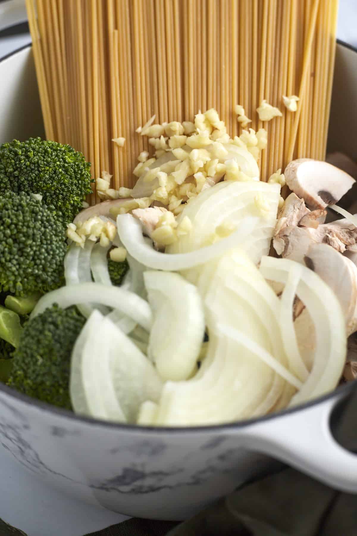 spaghetti noodles, garlic, onions, mushroom, and broccoli in a pot 