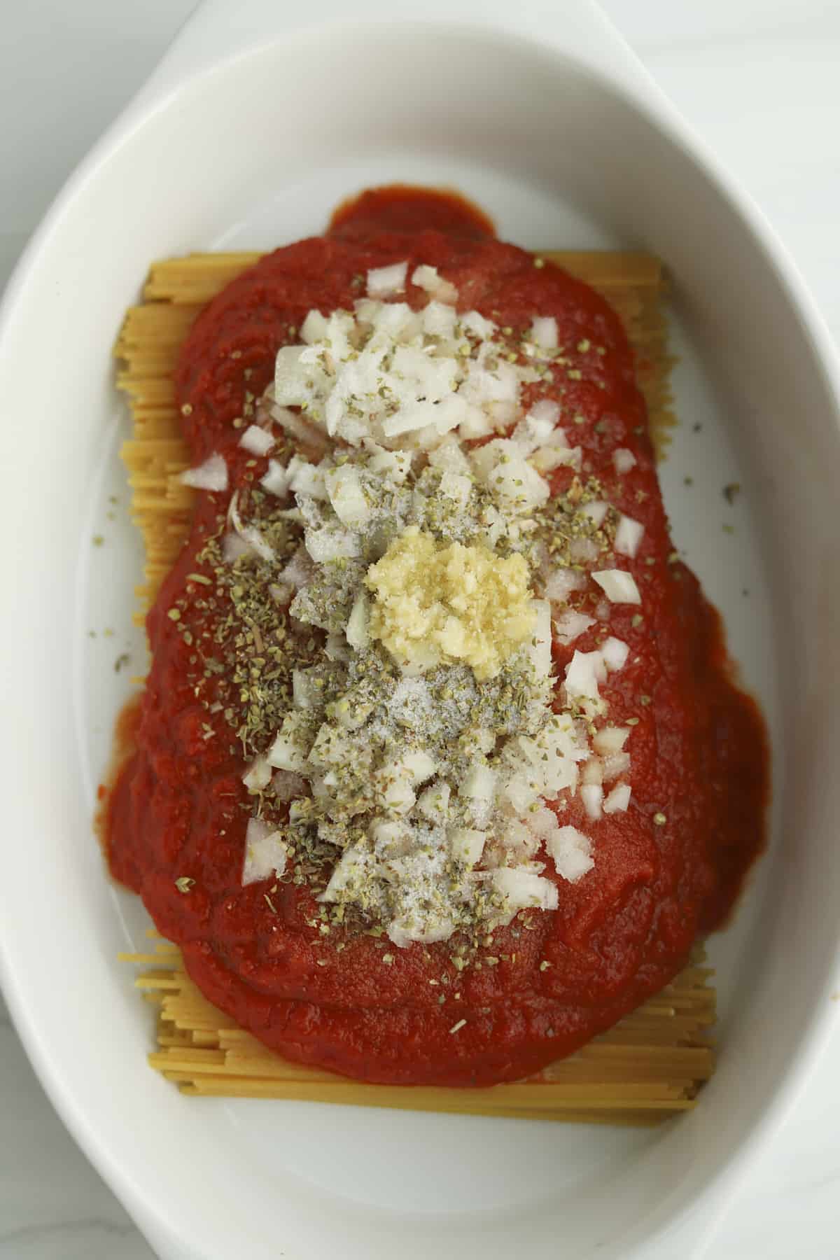 unbaked pot-sized spaghetti in a baking dish topped with marinara, onions, oregano, and garlic