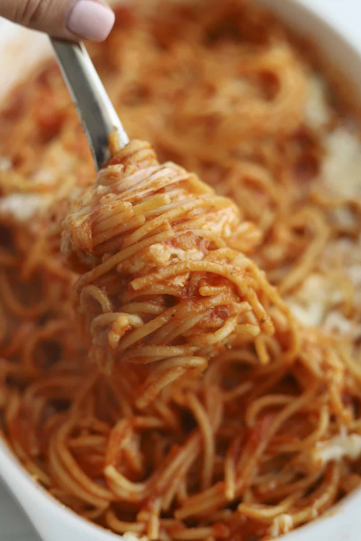large spoon full of spaghetti in a baking dish