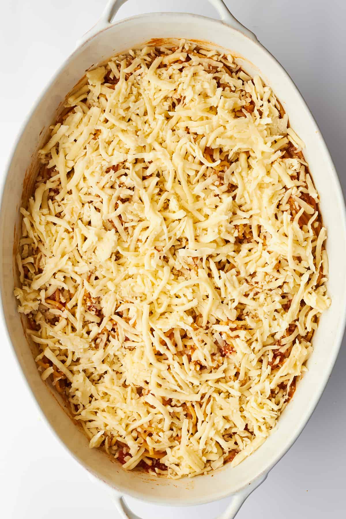 Cheese sprinkled over baked spaghetti in an oval dish. 