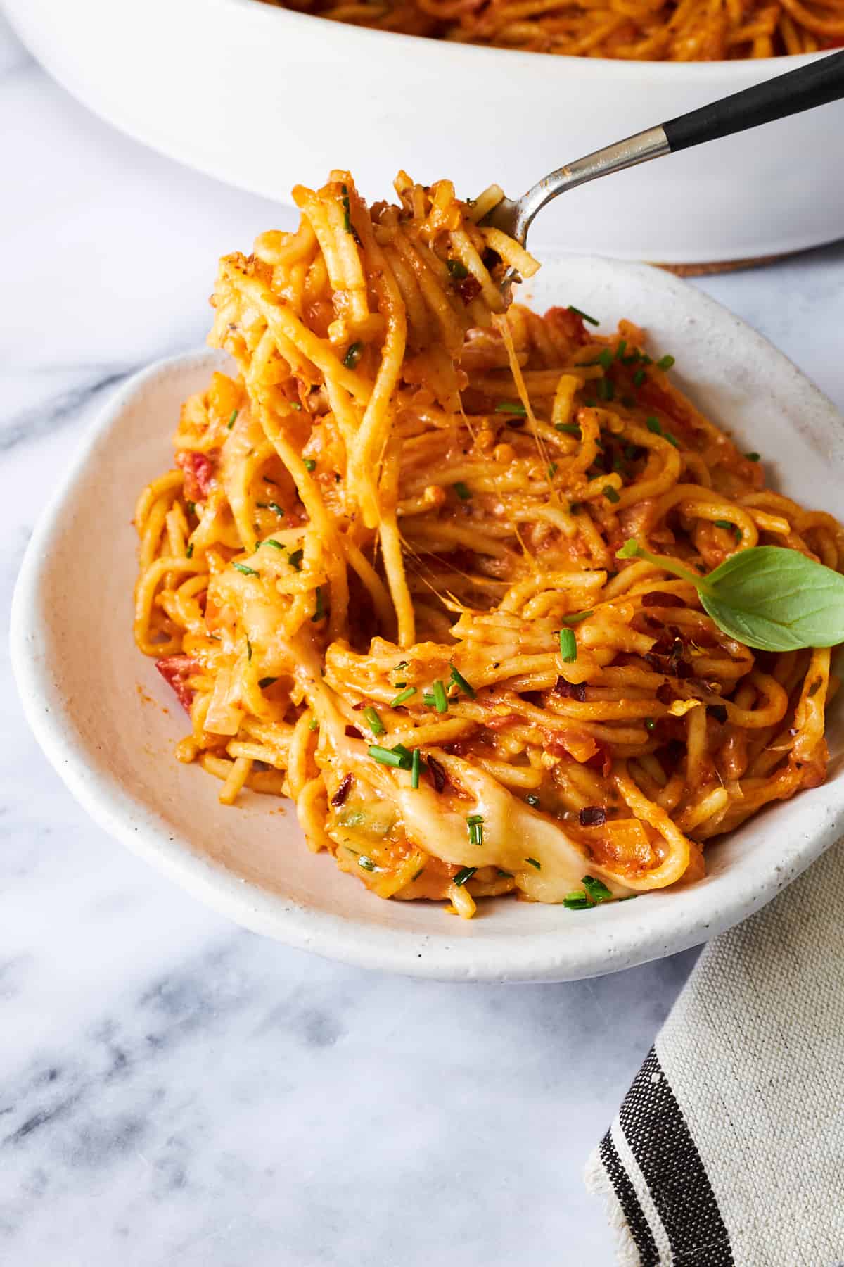 A fork lifting a bite of oven baked spaghetti on a plate.