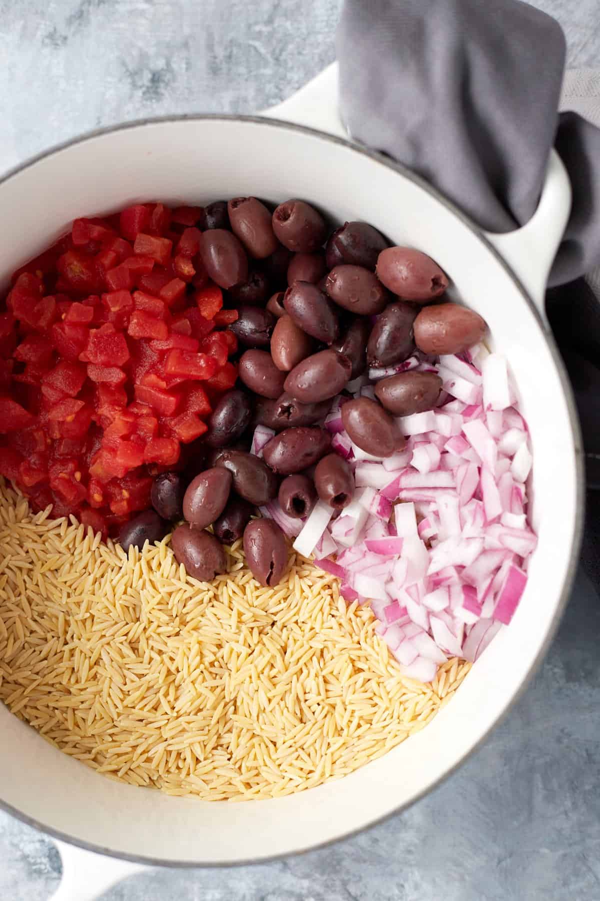 overhead of orzo pasta, olives, tomatoes and onions