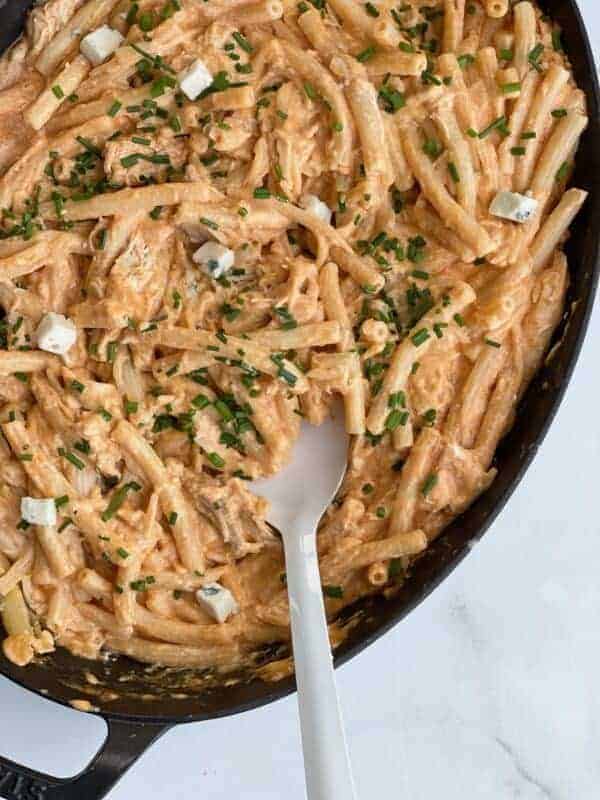 buffalo chicken pasta bake in a baking dish being stirred with a spoon