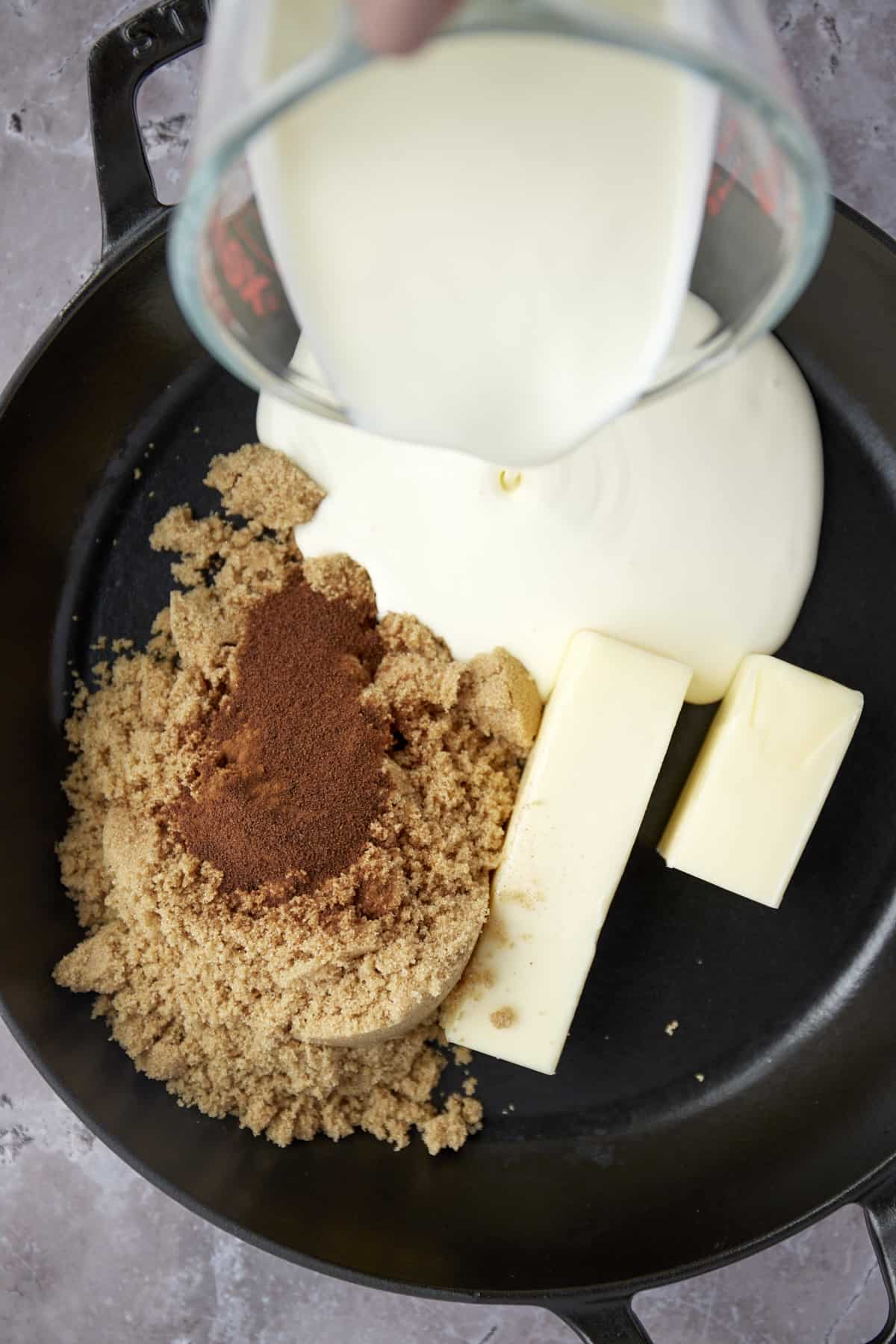 brown sugar, a stick and a half of butter, cinnamon, and heavy cream being poured into a skillet