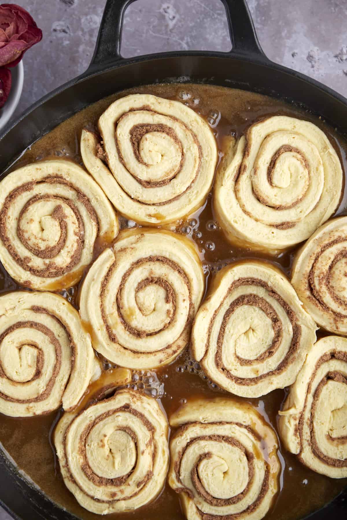 raw cinnamon rolls in a skillet with caramel sauce