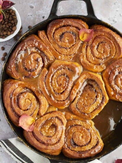 overhead image of a skillet of caramel macchiato cinnamon roll cake with a cinnamon roll missing