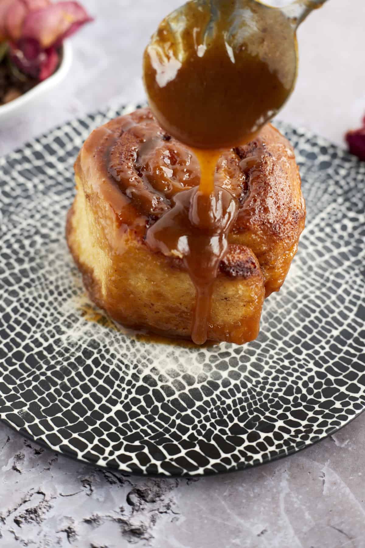 caramel sauce being drizzled over a caramel macchiato cinnamon roll on a plate