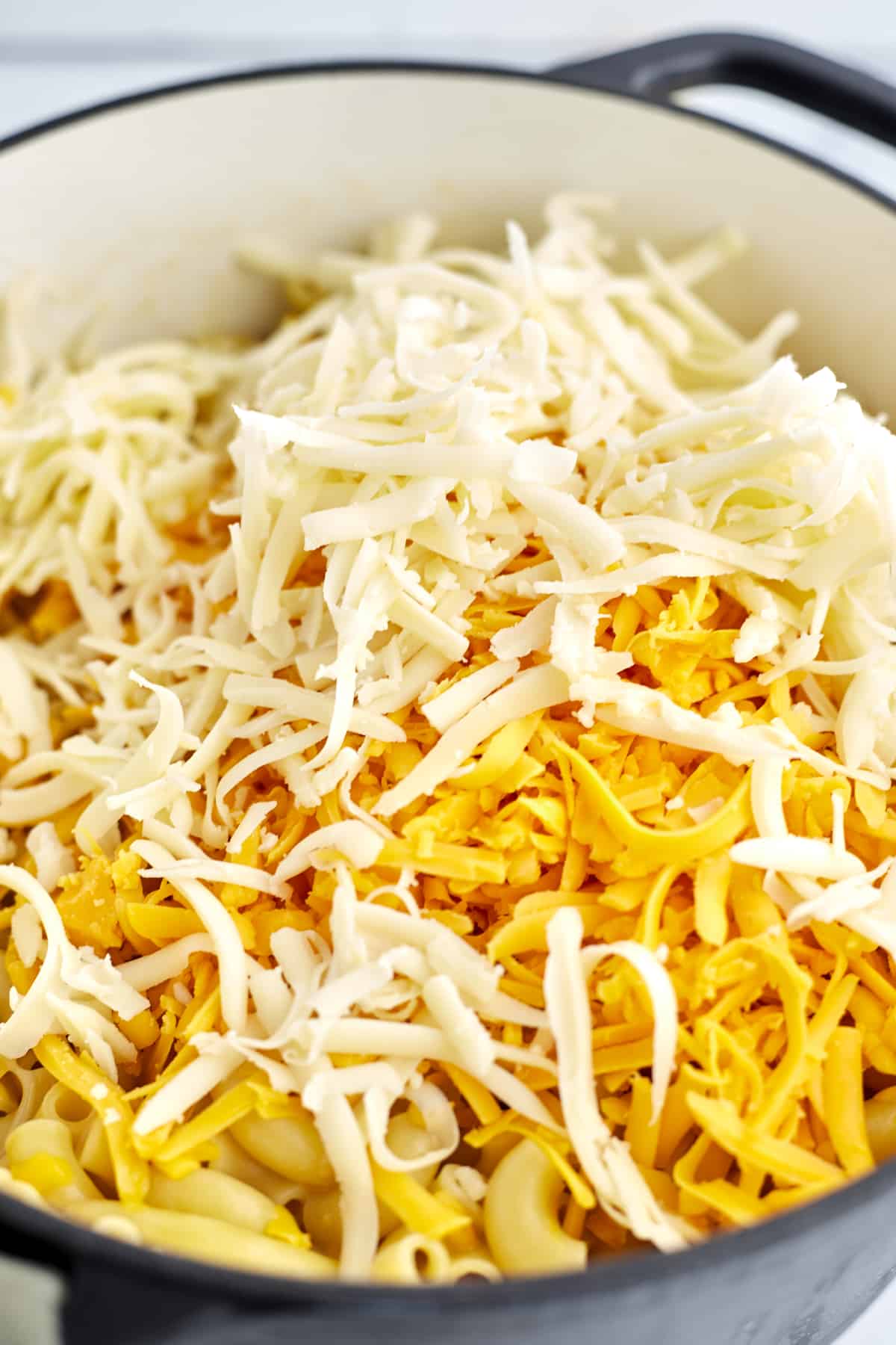 a large pot of cooked elbow pasta topped with shredded Cheddar and Mozzarella cheese