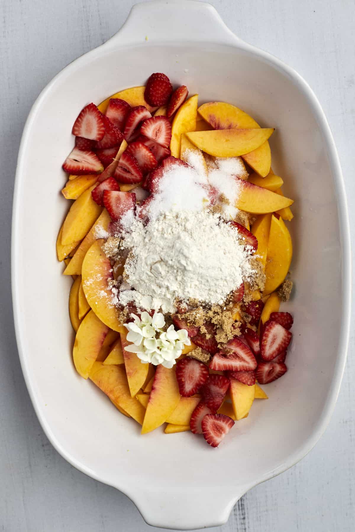 peaches and strawberries in a baking dish topped with with granulated sugar, brown sugar, cinnamon, and flour