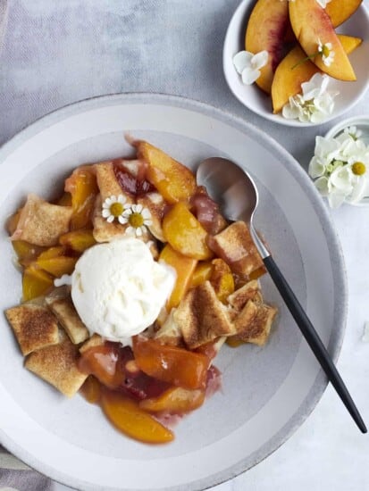overhead image of a bowl of peach strawberry cobbler topped with vanilla ice cream and a small bowl of peaches on the side