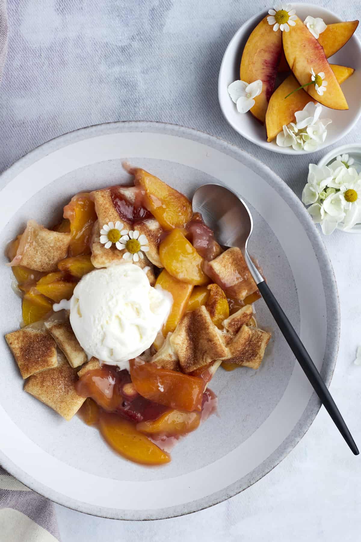 a bowl of easy peach strawberry cobbler topped with vanilla ice cream with a small bowl of peaches on the side
