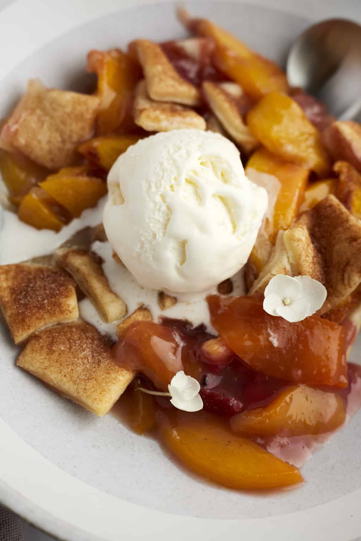 close up image of a serving of peach strawberry cobbler topped with a scoop of vanilla ice cream