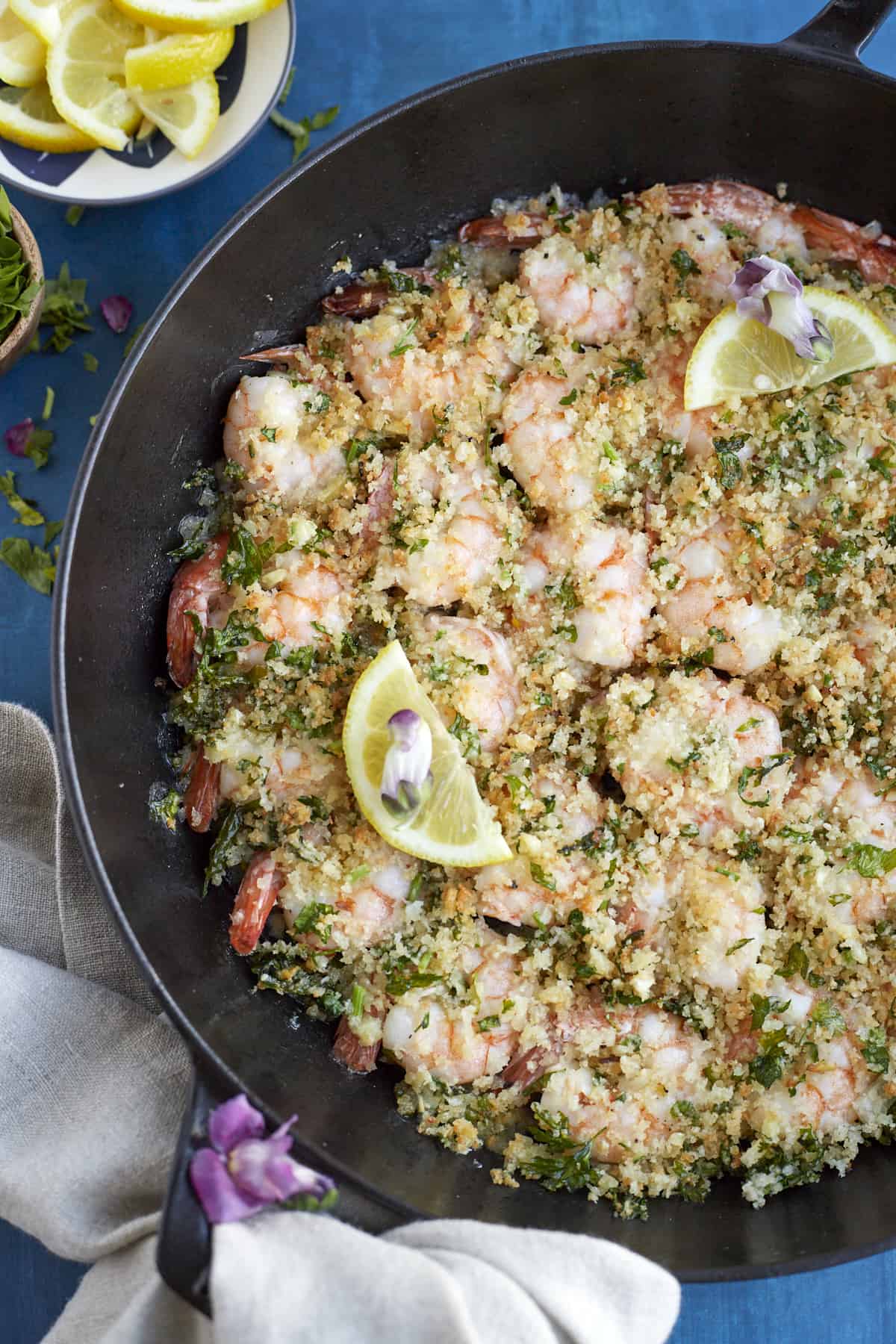 overhead image of baked shrimp scampi in a skillet topped with a lemon wedge