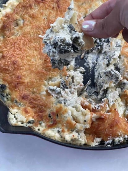 a hand dipping a chip into creamy chicken spinach and artichoke dip