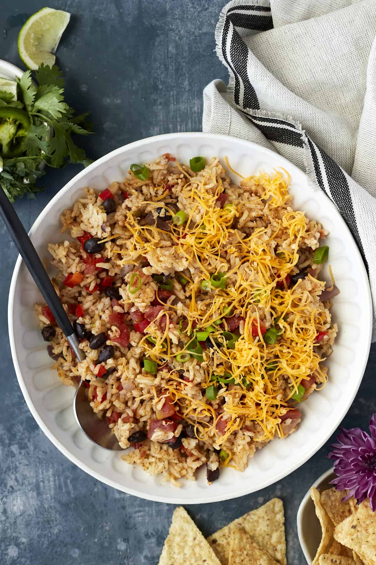 Overhead image of a white plate full of easy Mexican rice recipe with veggies and cheese with a black spoon on the side