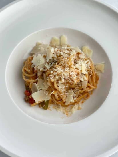 A plate with a serving of baked spaghetti bolognese recipe topped with shaved parmesan.