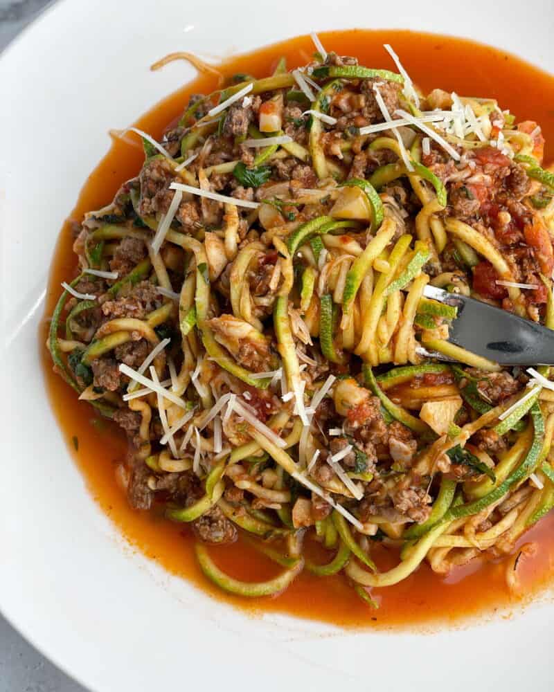 low carb baked spaghetti zoodles toped with Parmesan in a white pasta bowl being twirled with a fork