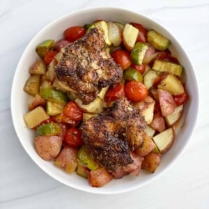 overhead image of a white bowl full of Sheet Pan Chicken Thighs and Veggies