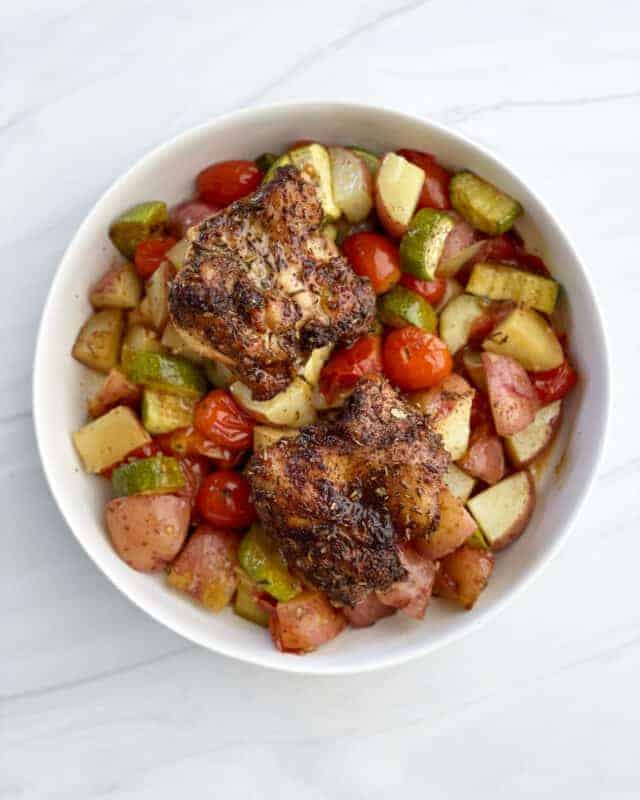 overhead image of a white bowl full of Sheet Pan Chicken Thighs and Veggies.