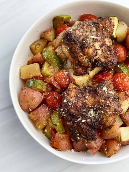 a close up image of a bowl full of cooked seasoned chicken thighs on top of a bed of veggies.