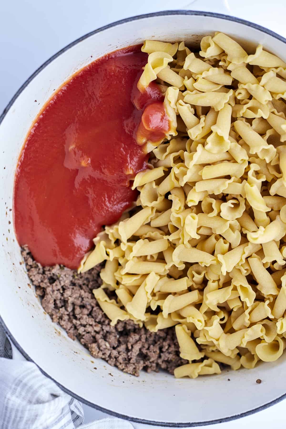 cooked ground beef with sauce and uncooked pasta in a pot.
