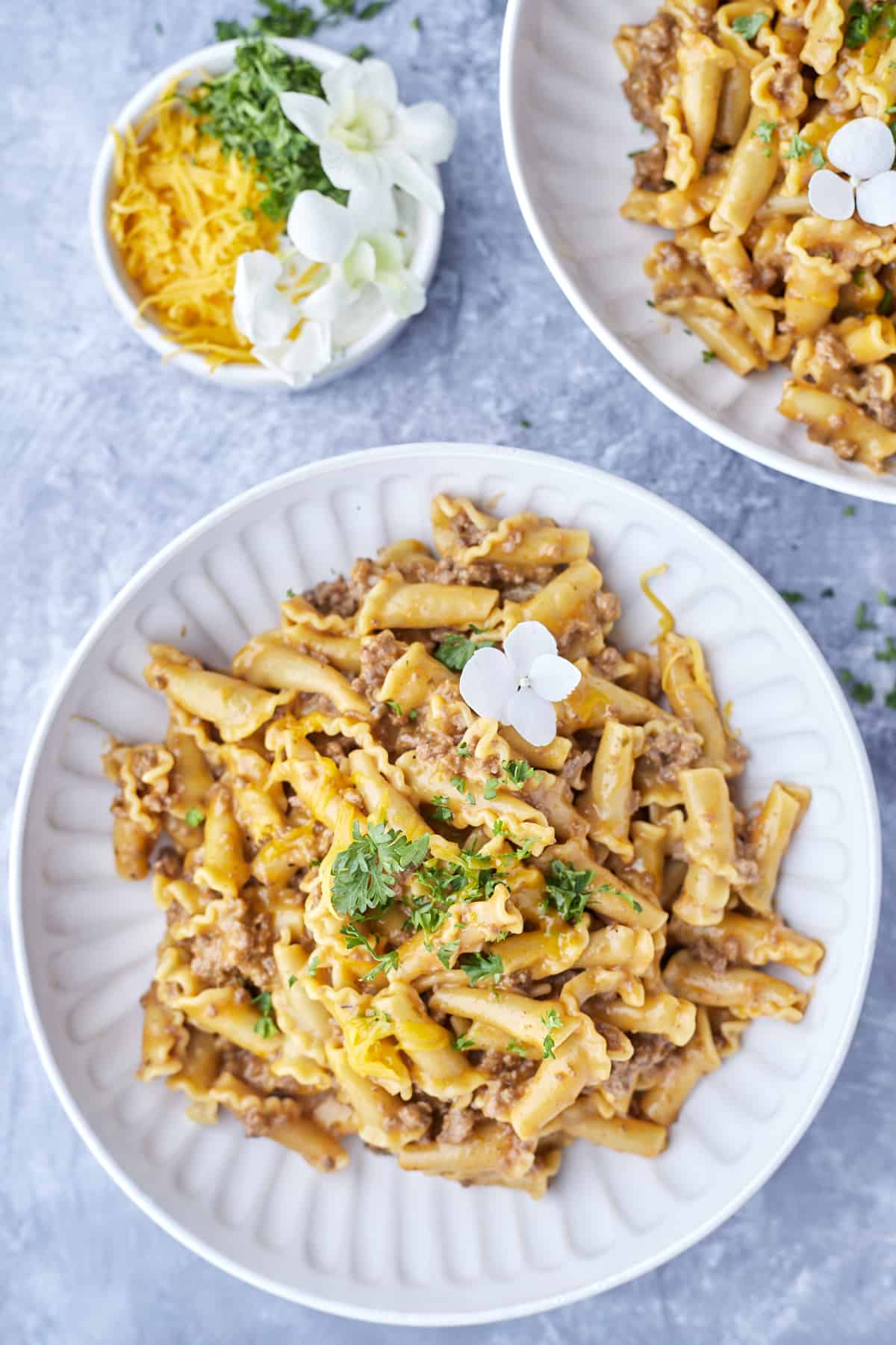 two plates of one pot cheeseburger pasta with a bowl of shredded cheese to the side