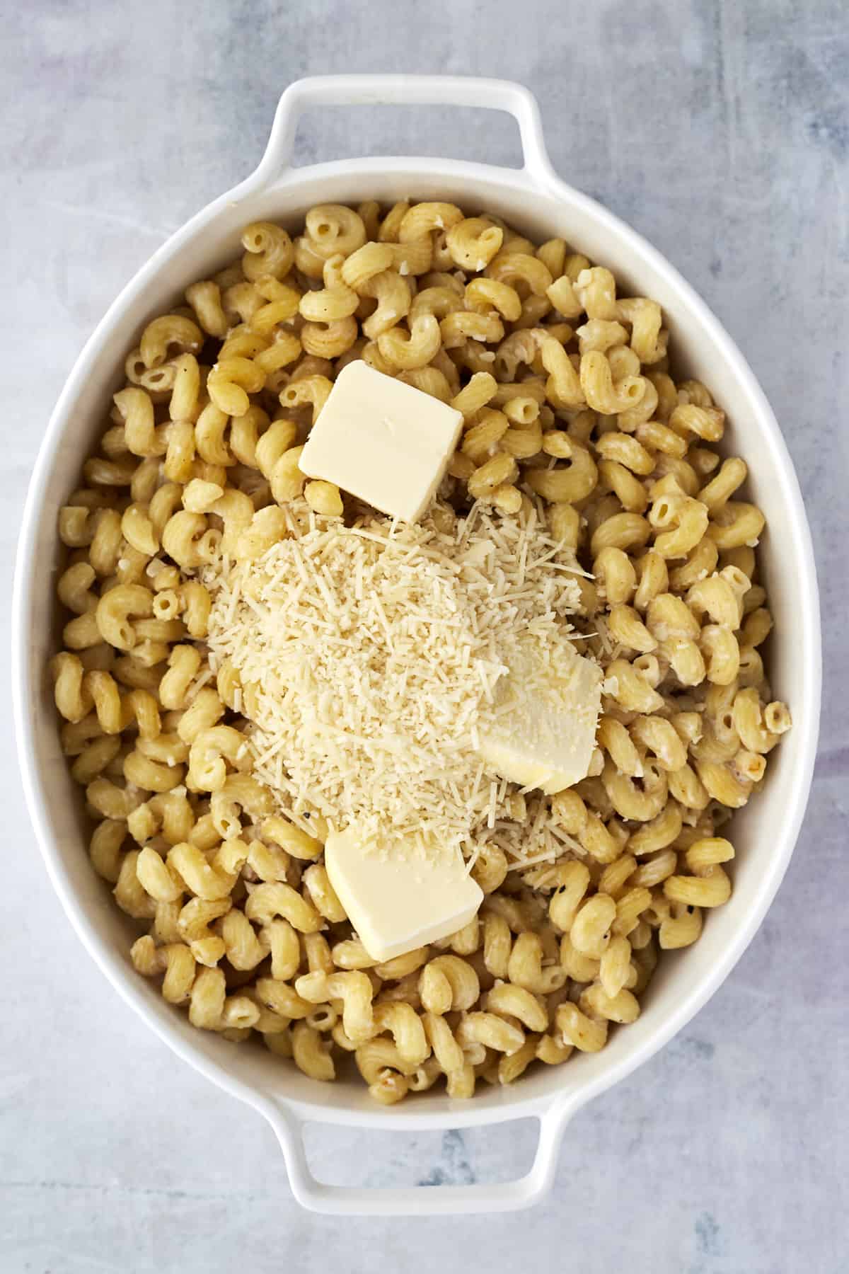 butter and cheese on top of cavatappi noodles in an oval baking dish 