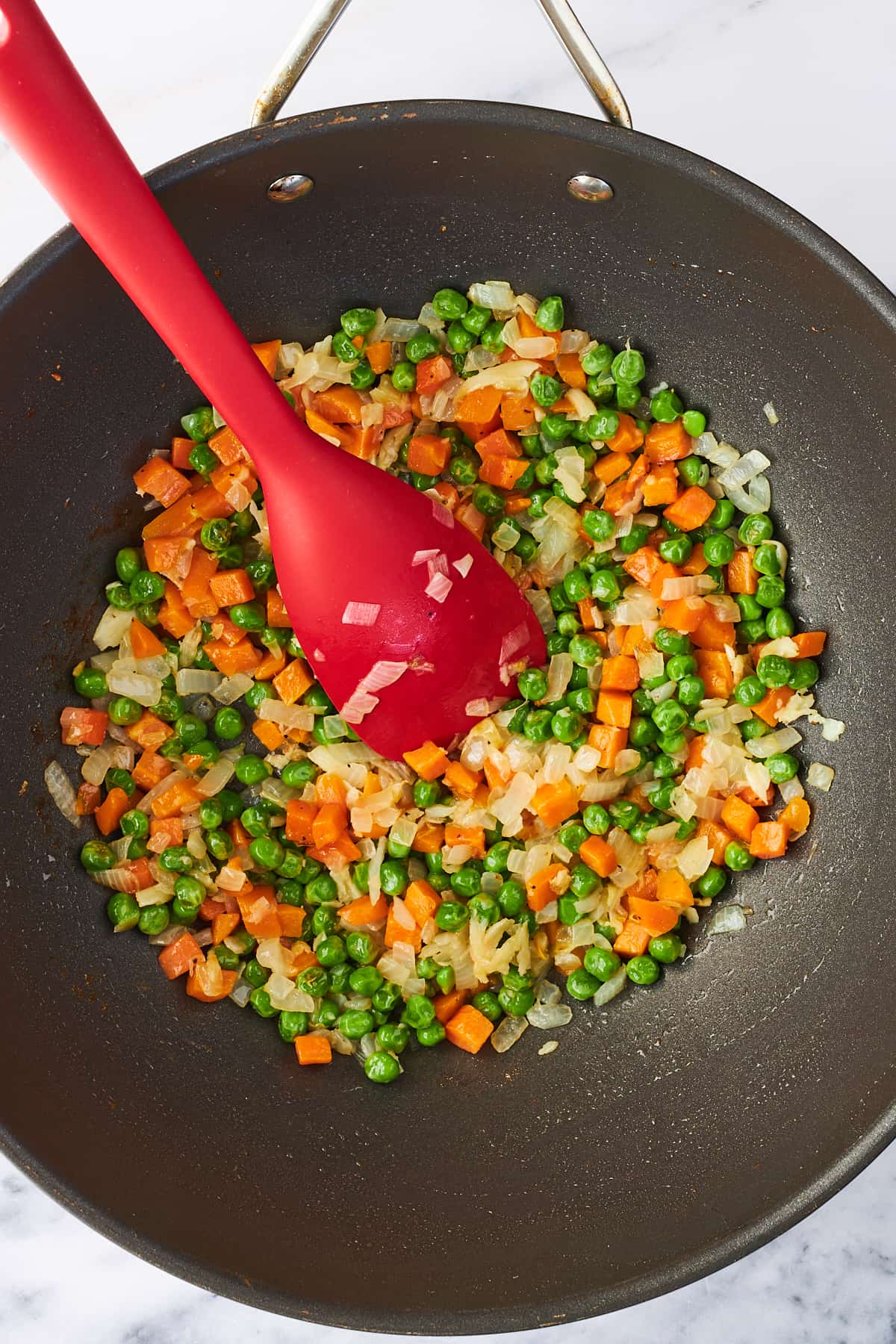 A spatula stirring sautéeing veggies for egg fried rice in a wok. 