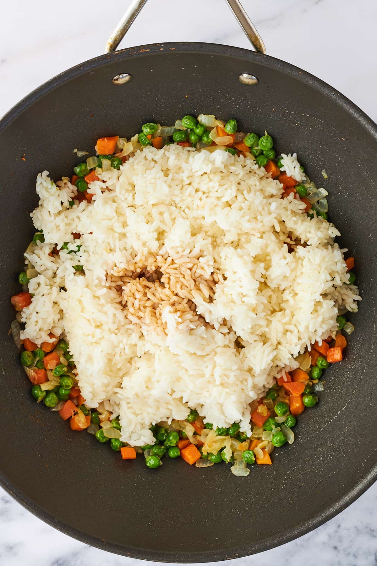 Rice and soy sauce being added to veggies in a wok. 