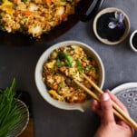 Chopsticks being held over a bowl of wok fried rice.