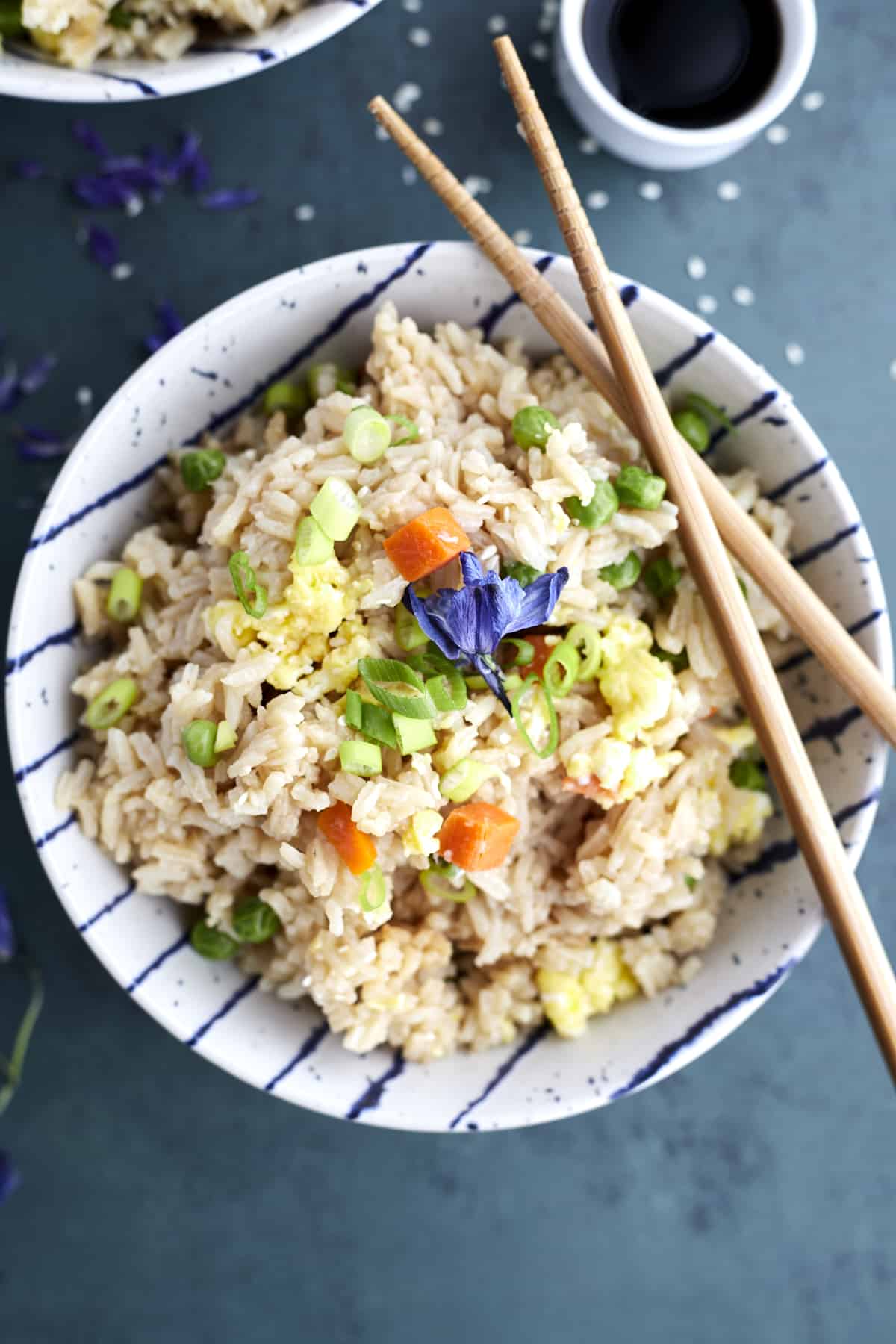Overhead image of a bowl of easy fried rice with veggies with two chopsticks balanced on top and a side of soy sauce 