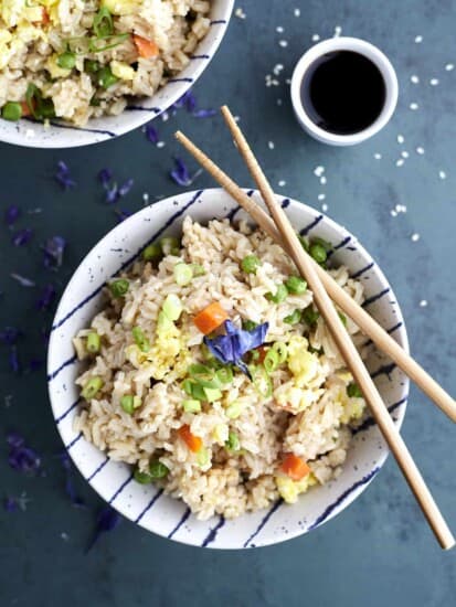 a bowl of easy fried rice with veggies with chopsticks on top and a small bowl of soy sauce on the side