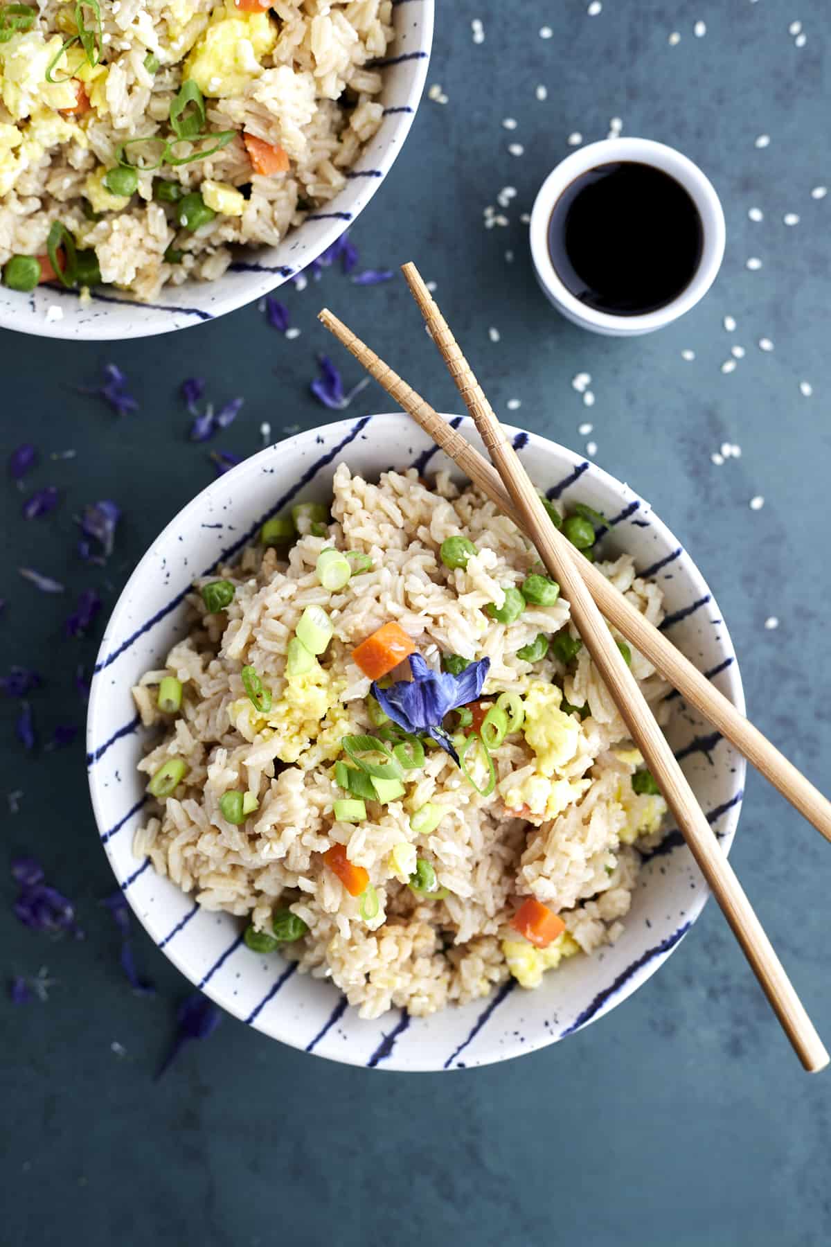 A bowl of easy fried rice with veggies with two chopsticks balanced on top and a side of soy sauce