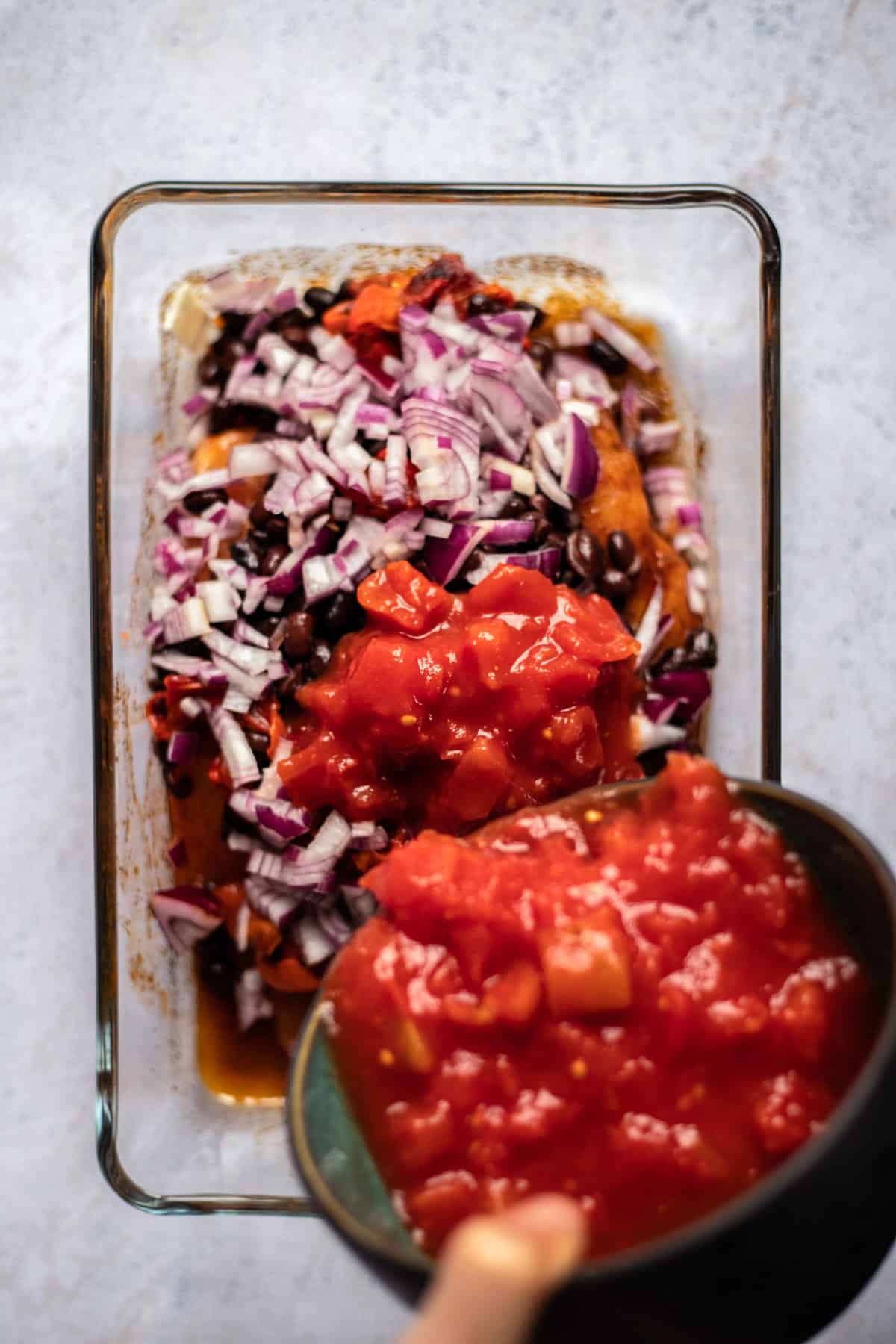 raw seasoned chicken topped with black beans and diced red onions with  salsa being poured on top