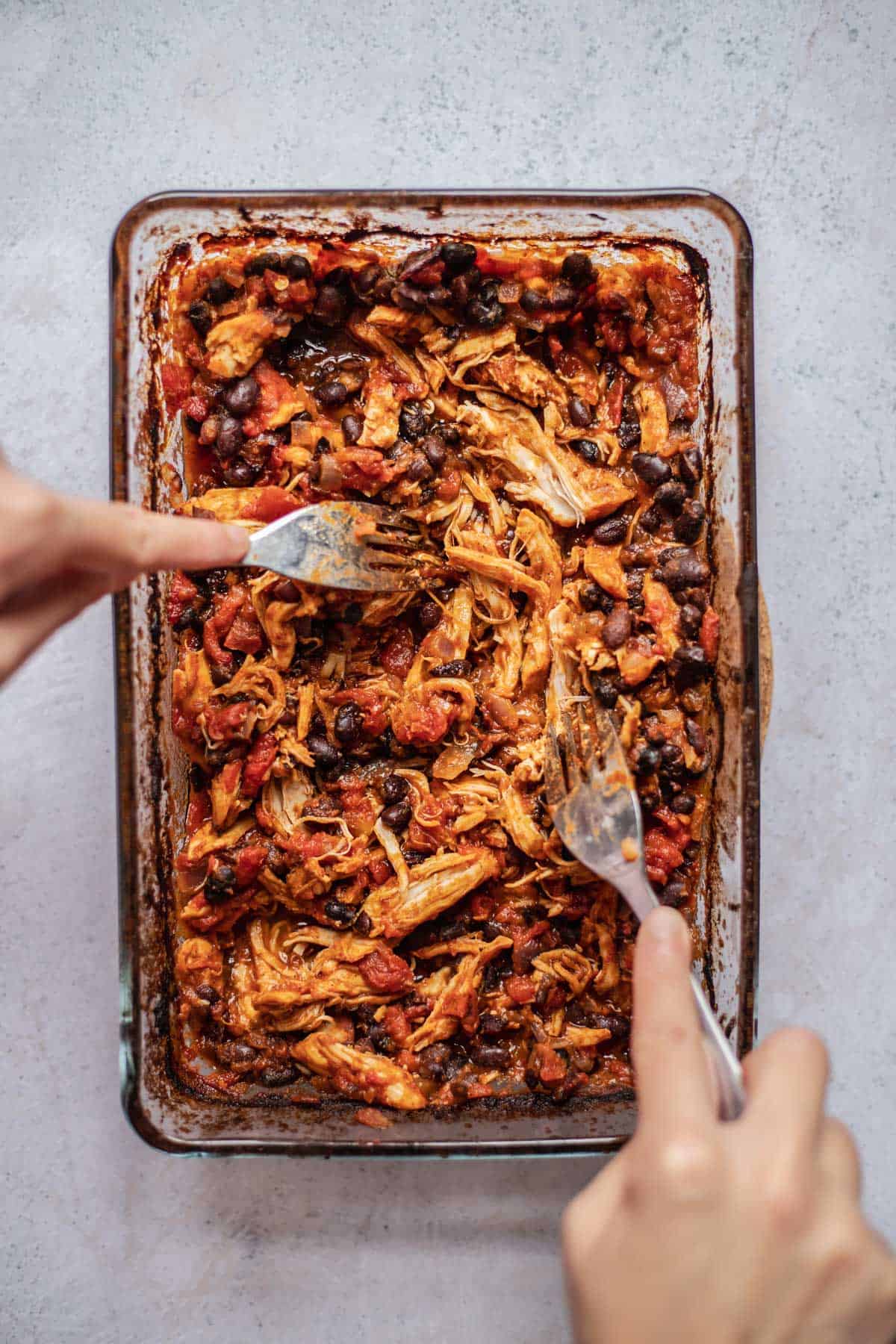 two hands using forks to shred chicken taco meat