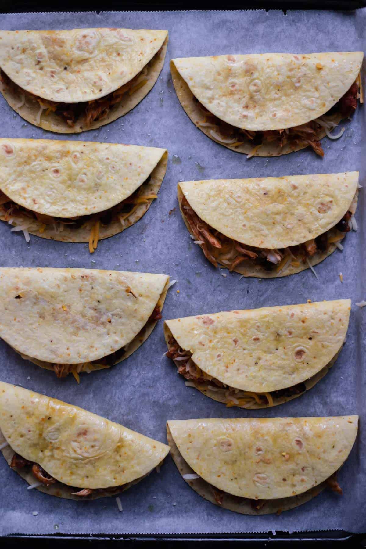 taco shells stuffed with shredded chicken on a parchment-lined baking sheet