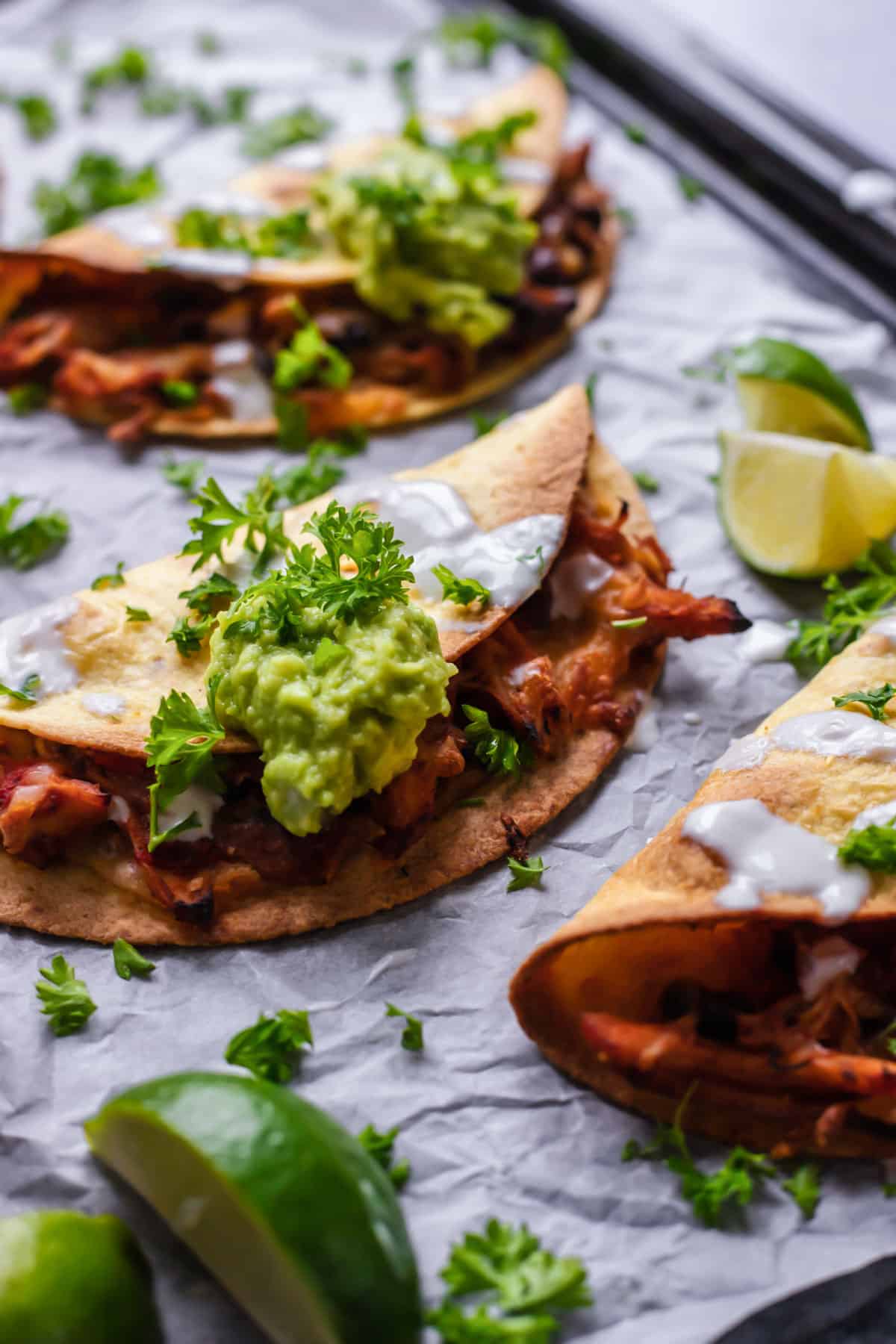 close up image of baked shredded chicken tacos topped with guacamole and fresh herbs