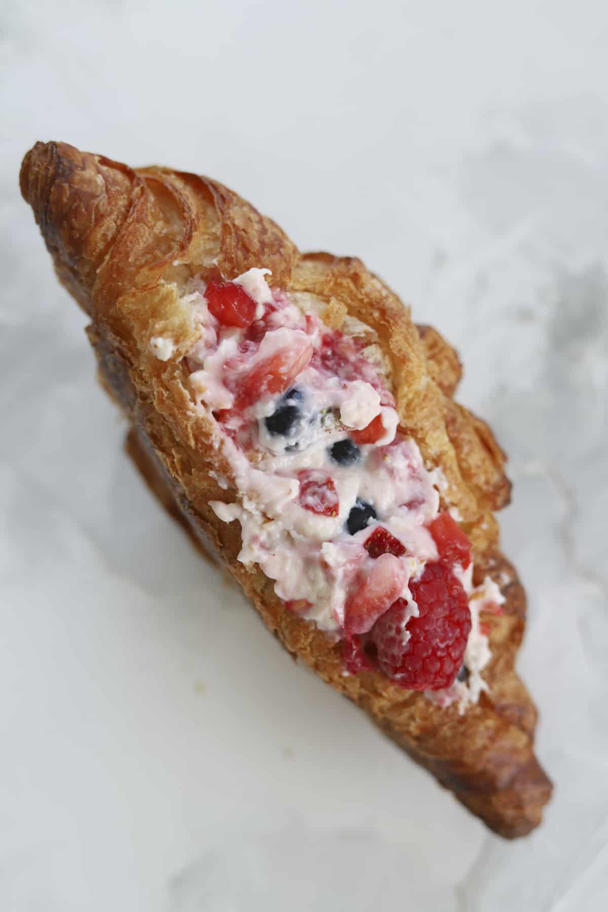 overhead of one croissant stuffed with berries and cream cheese