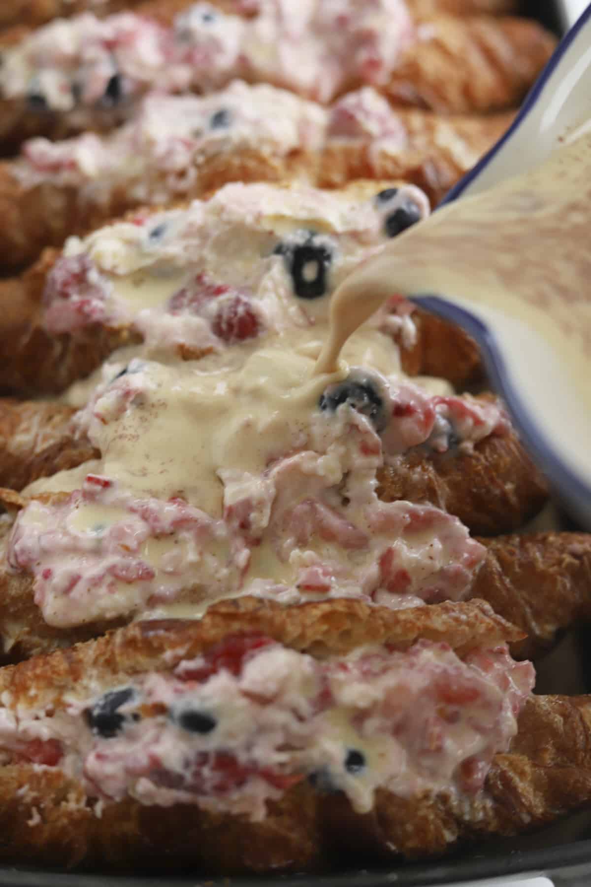 side view of berry stuffed croissant french toast with pouring of custard