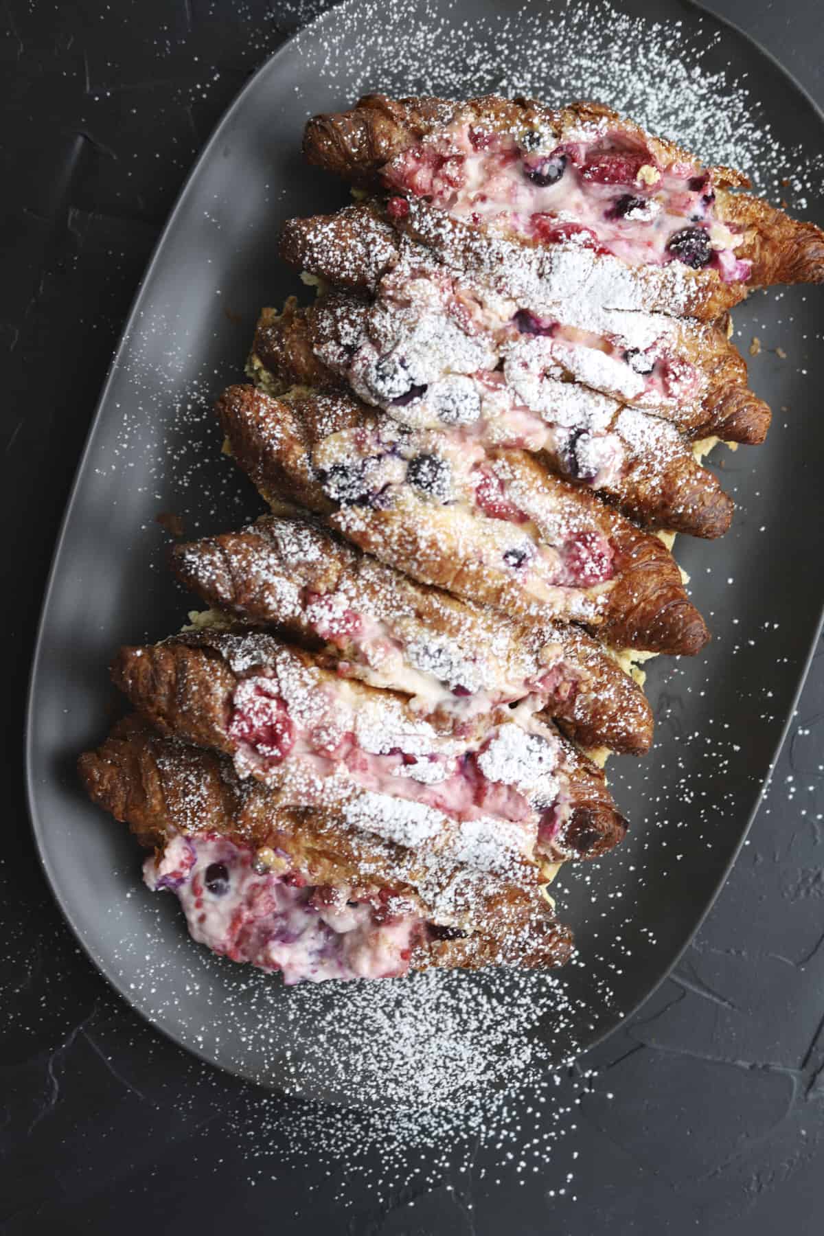 overhead berry stuffed croissant french toast on a platter with powdered sugar