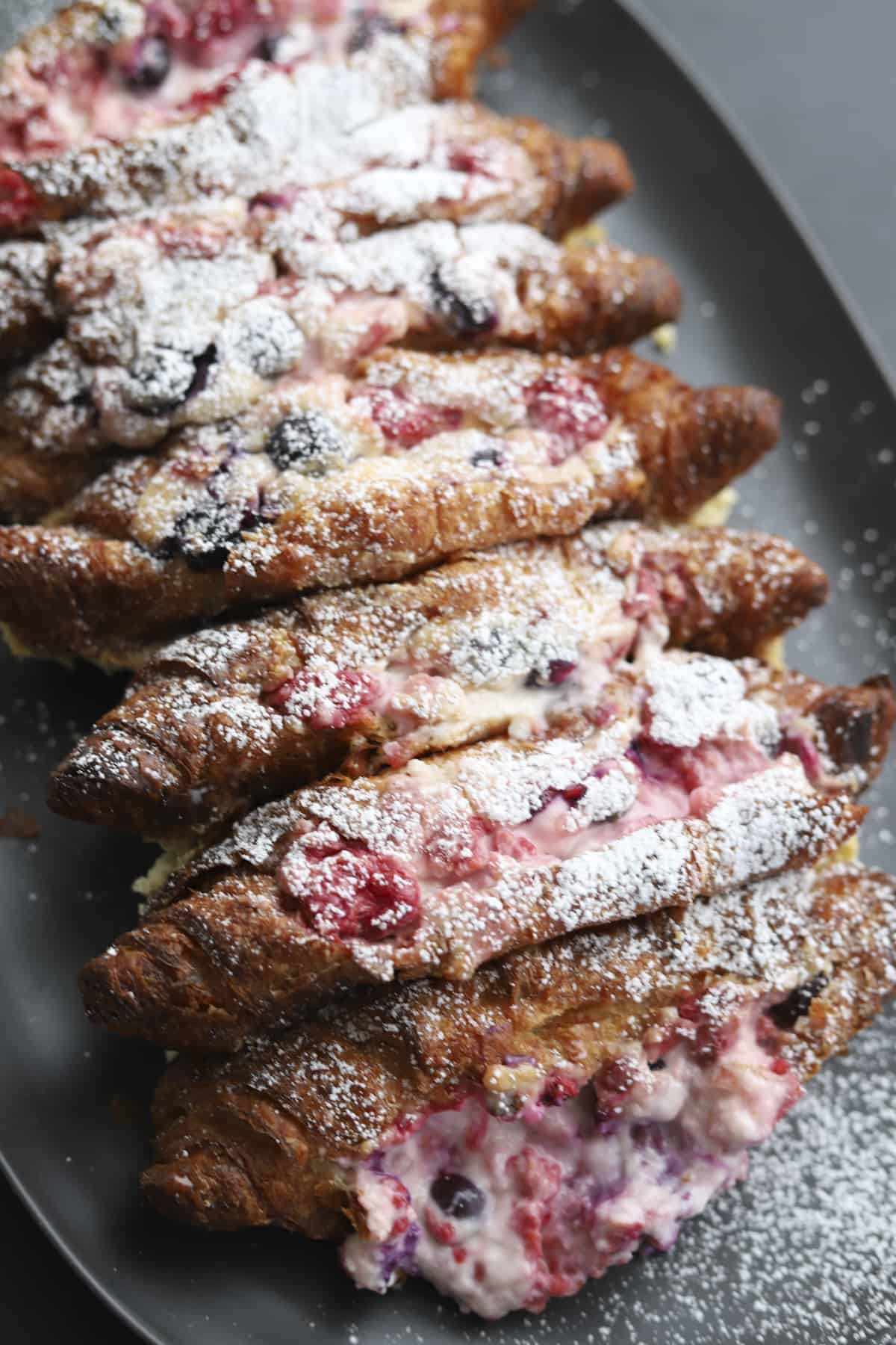 overhead berry stuffed croissant french toast on a platter with powdered sugar